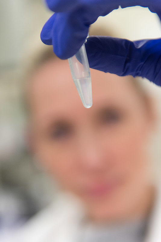 A women looks at a small test tube filled with clear liquid.